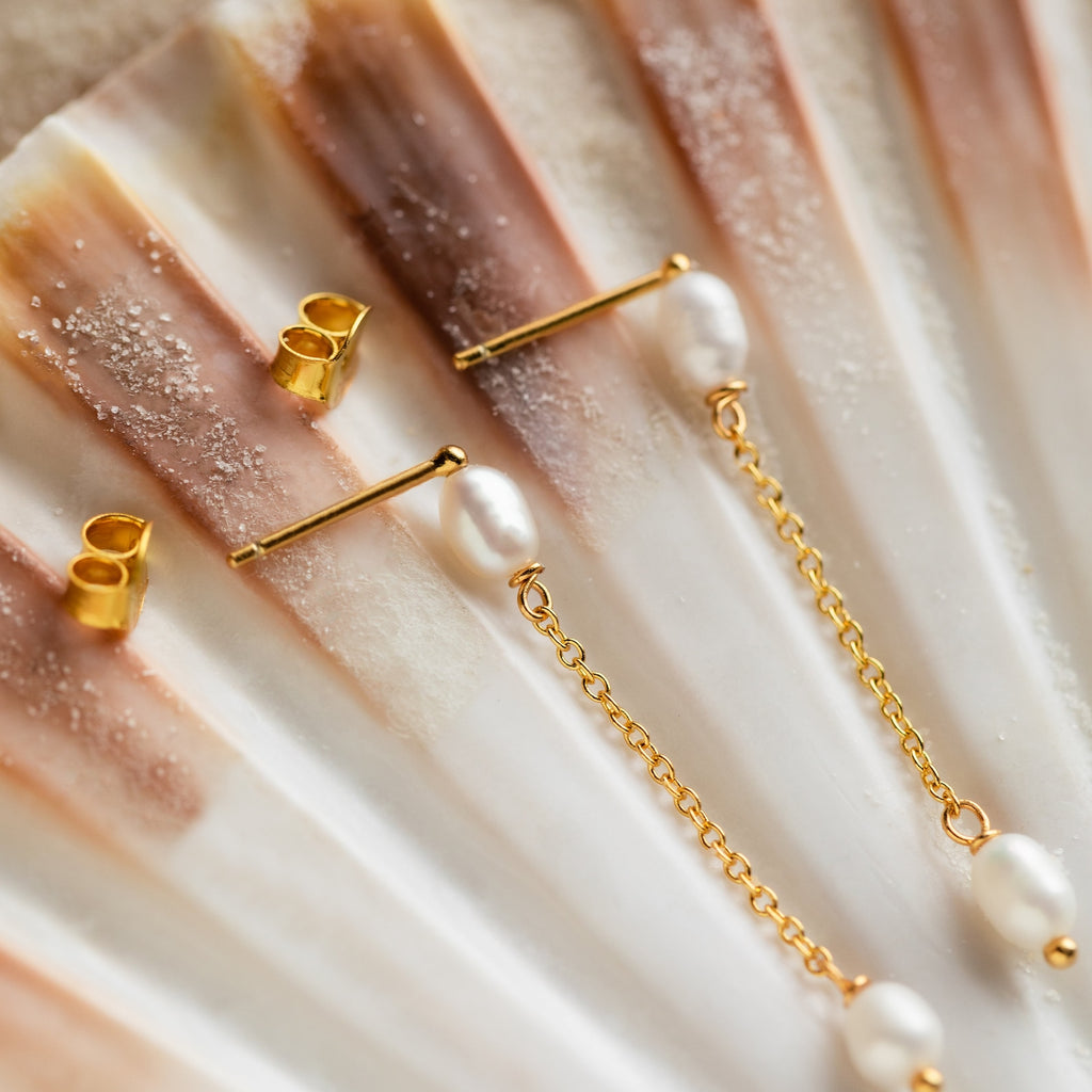 Pearl Drop Chain Earrings with butterfly backs are shown on a ridged seashell background, emphasizing their minimalist elegance.