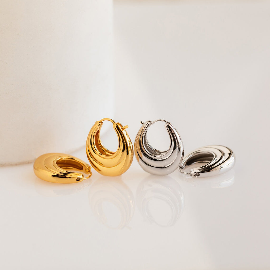 Two pairs of Katrina Ribbed Hoops—one gold, one silver—showcasing a modern chunky ribbed design are beautifully displayed on a white surface.
