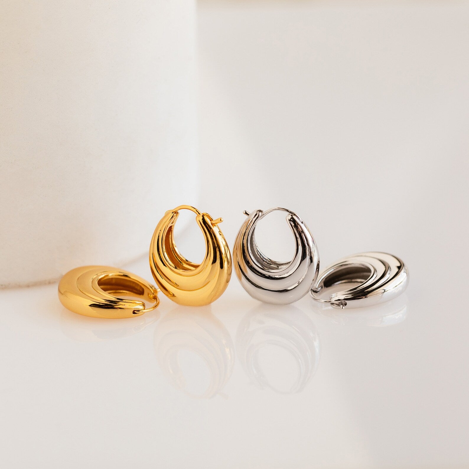 Two pairs of Katrina Ribbed Hoops—one gold, one silver—showcasing a modern chunky ribbed design are beautifully displayed on a white surface.