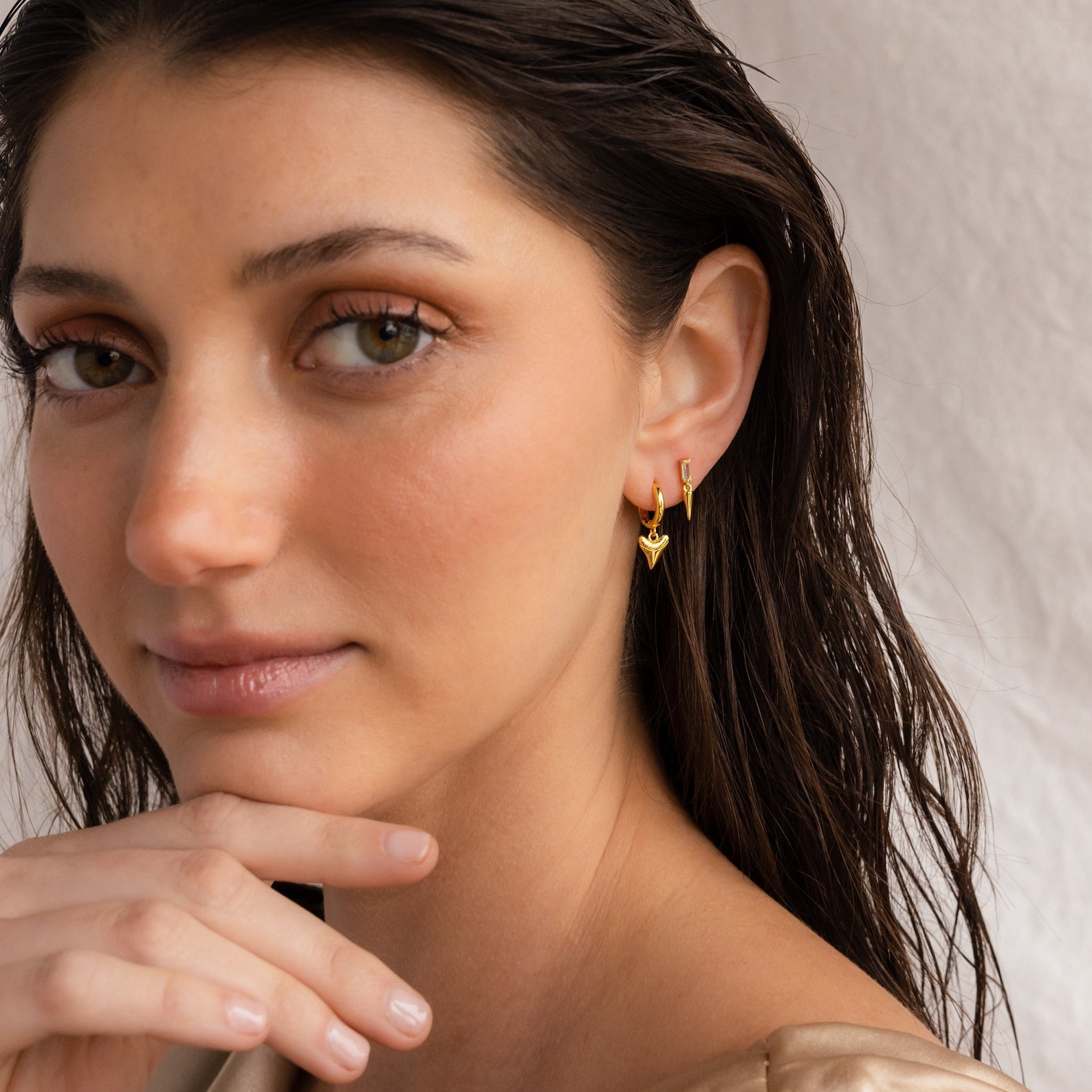 A woman with her hand on her chin, showcasing stylish Shark Tooth Huggies that add a unique twist to her beach jewelry look.