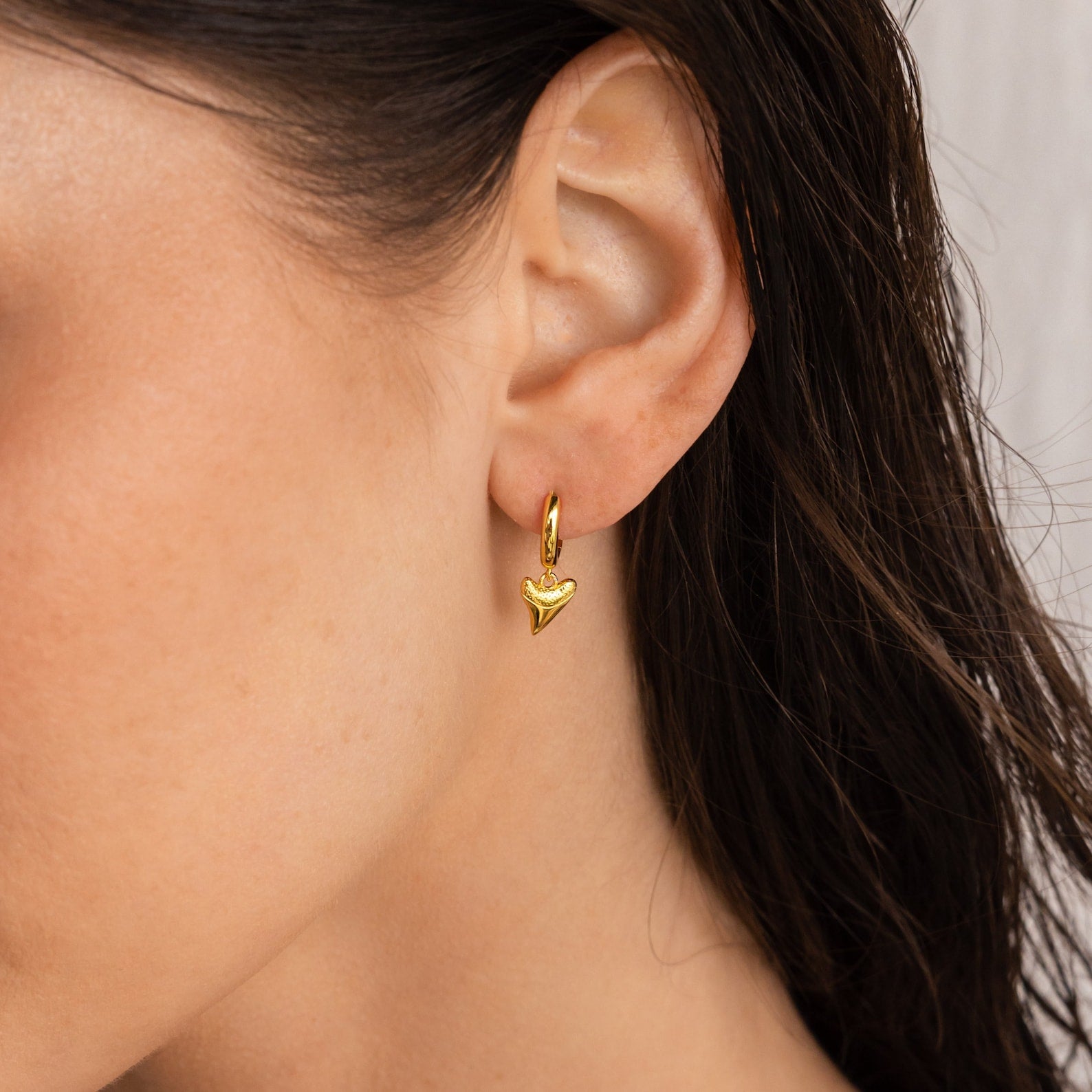 Close-up of a woman's ear wearing Shark Tooth Huggies, small gold hoop earrings with a shark tooth charm, ideal for beach jewelry fans.