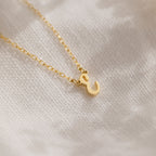 The Stylish Dainty Initial Necklace, featuring a gold ampersand pendant, is displayed on soft, white textured fabric.