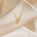 The Grace Dainty Initial Necklace features a custom cursive initial pendant on a gold chain, elegantly displayed on soft, cream-colored fabric.
