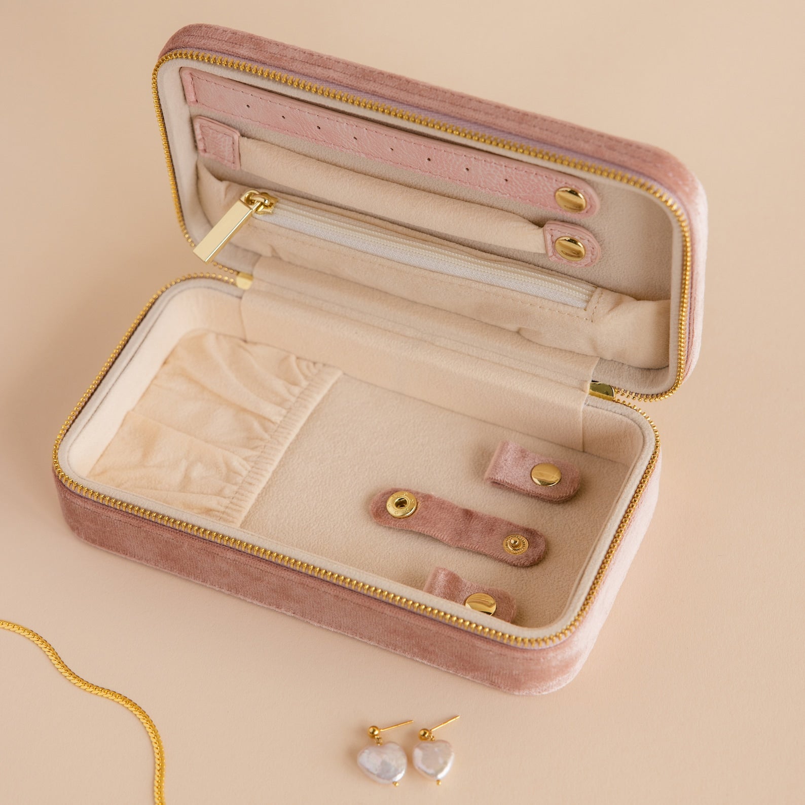Rectangle Velvet Jewelry Case in pink shown open on a beige surface, displaying earrings, a necklace, and featuring a visible gold zipper detail.