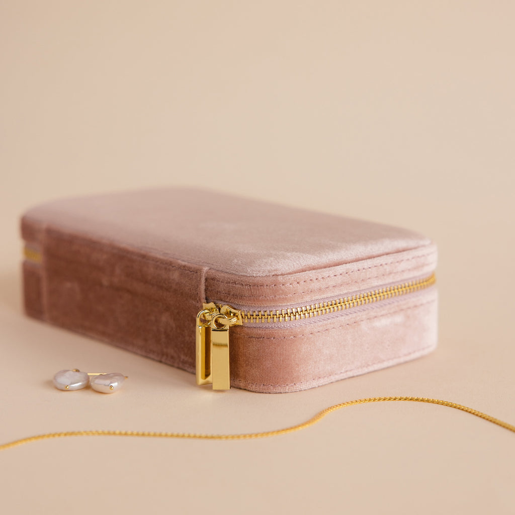 The Rectangle Velvet Jewelry Case in blush pink velvet with a gold zipper is shown beside pearl earrings and a gold chain necklace.