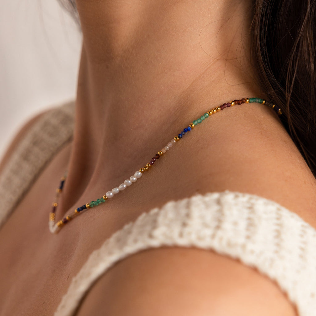 A close-up of a woman's neck wearing the Oasis Rainbow Beaded Necklace, a vibrant summer accessory, paired with a cream knit top.