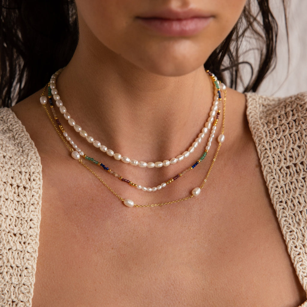 A woman wearing the Oasis Rainbow Beaded Necklace, a layered boho accessory featuring colorful beads, paired with a crocheted beige top—perfect for summer style.