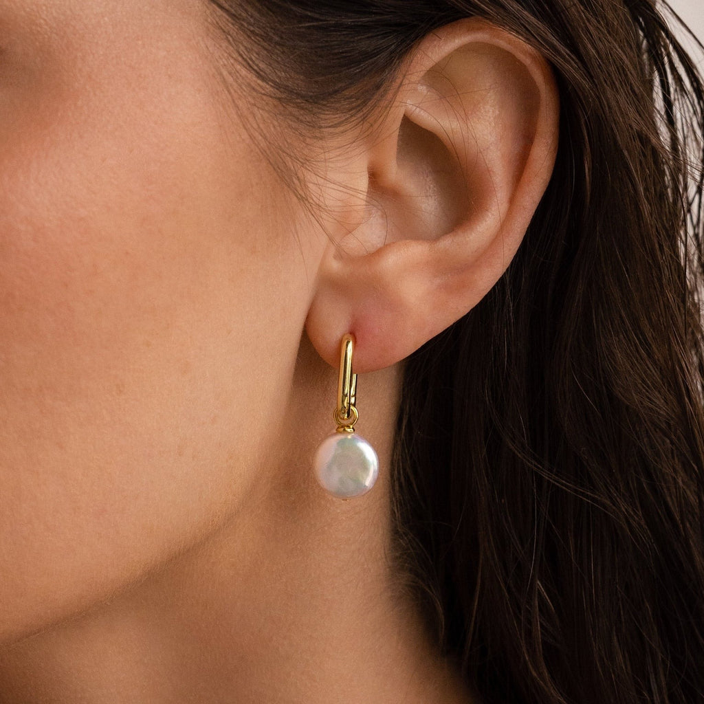 A close-up of a woman’s ear adorned with elegant Bridget Pearl Hoops, featuring delicate pearl charms.