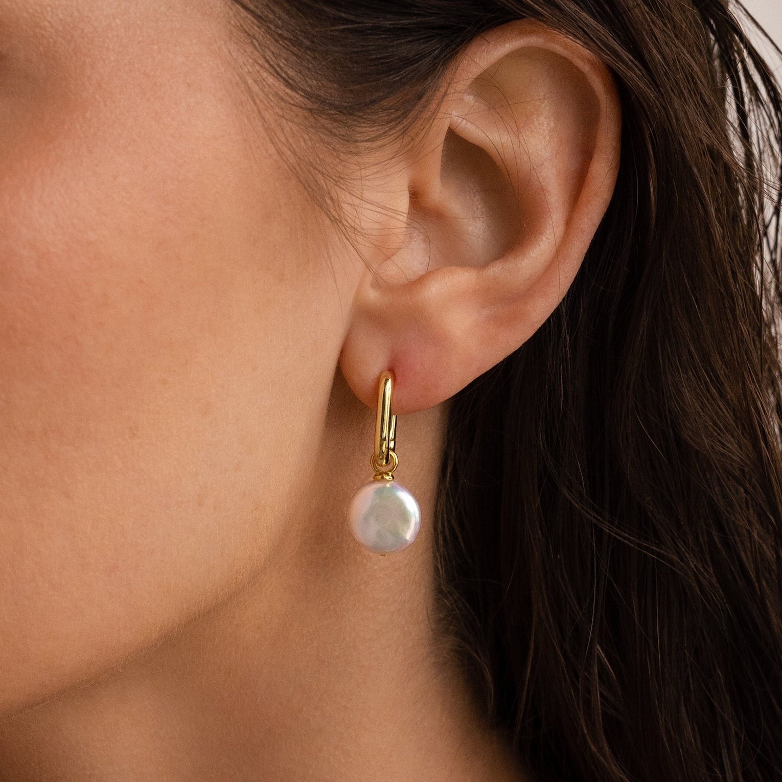 A close-up of a woman’s ear adorned with elegant Bridget Pearl Hoops, featuring delicate pearl charms.