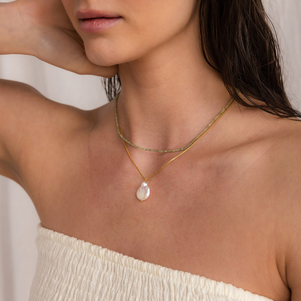 Woman wearing a white off-shoulder top, styled with Boho Beaded Necklaces—gold chains and a pearl pendant add the perfect finishing touch to trendy summer outfits.