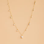 The Baroque Pearl Station Necklace in 18K Gold features a gold chain with spaced white pearls, displayed on a light beige background—an elegant choice for wedding jewelry.