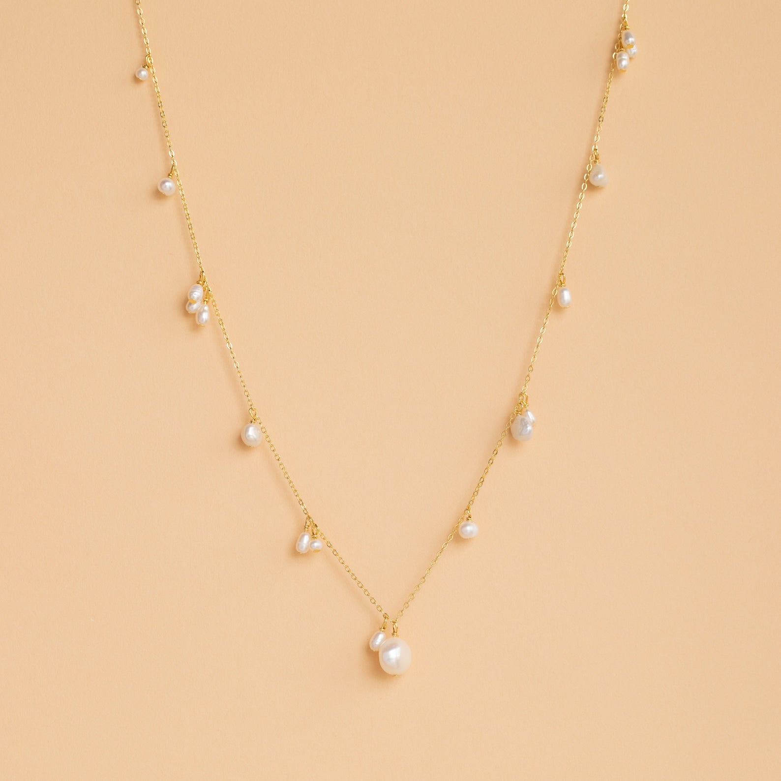 The Baroque Pearl Station Necklace in 18K Gold features a gold chain with spaced white pearls, displayed on a light beige background—an elegant choice for wedding jewelry.