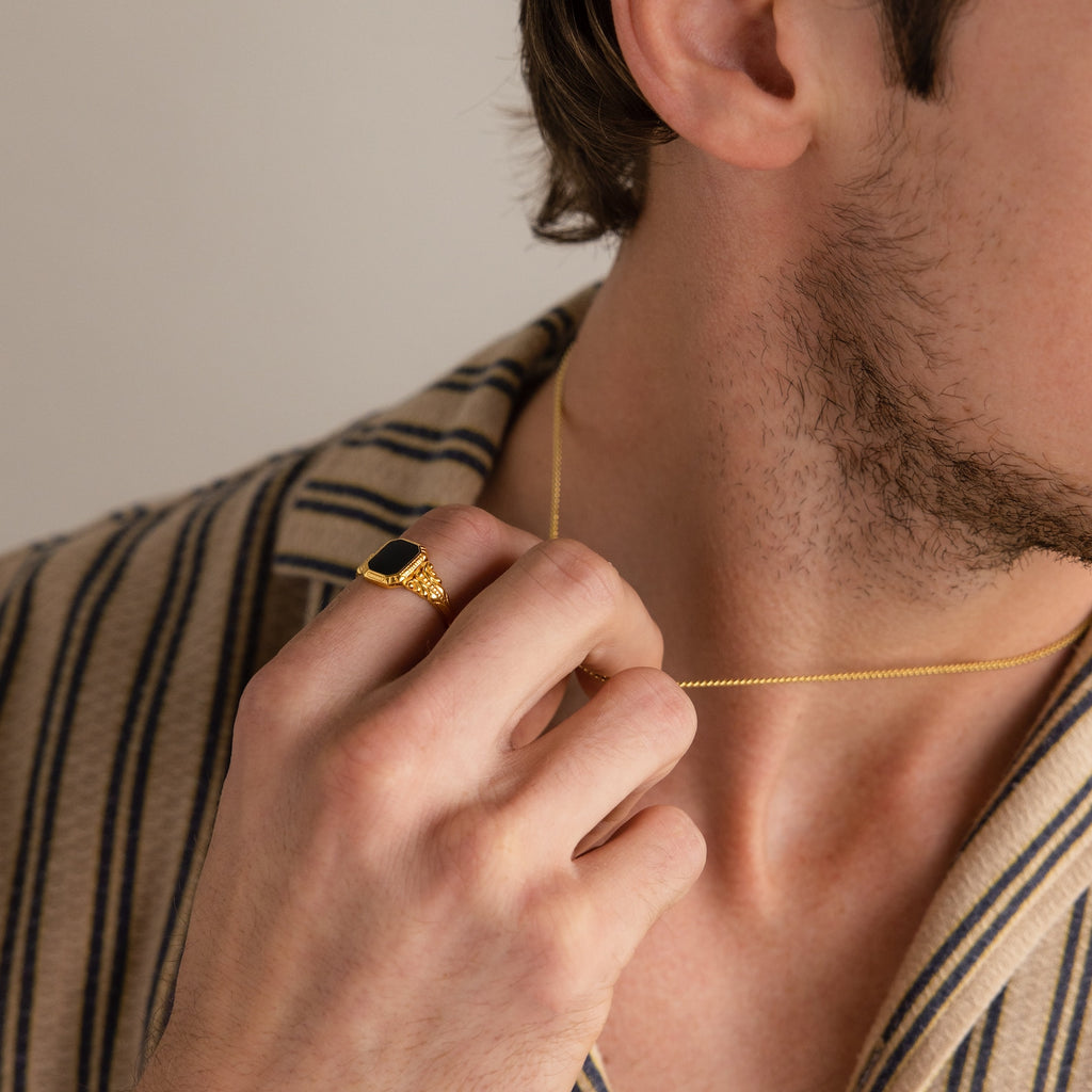 A man in a striped shirt holds a gold necklace and wears the Vintage Black Signet Ring.