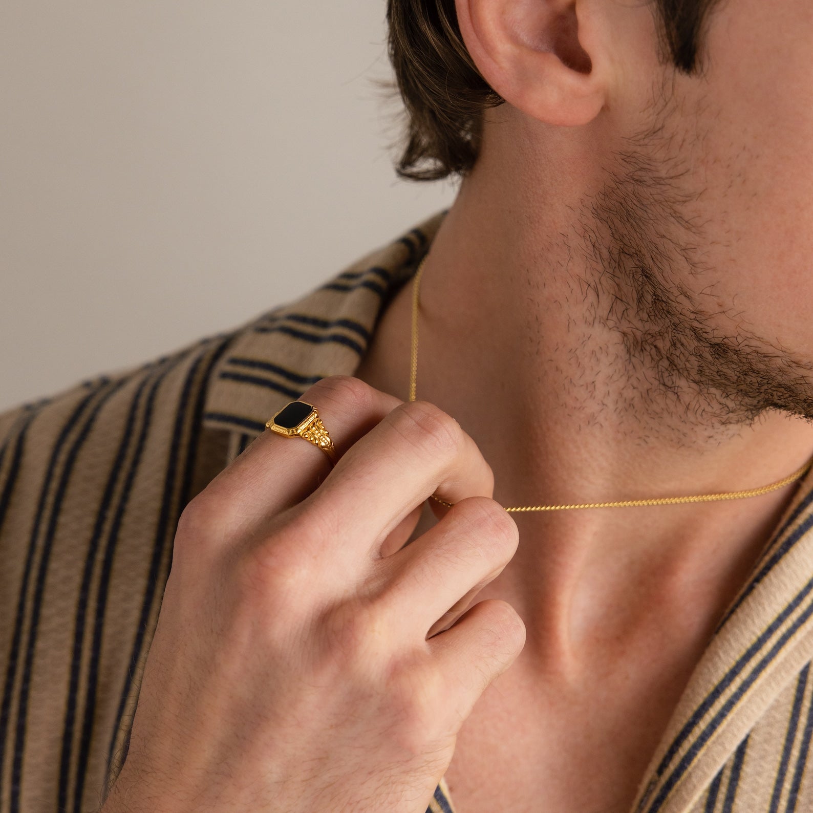 A man in a striped shirt holds a gold necklace and wears the Vintage Black Signet Ring.