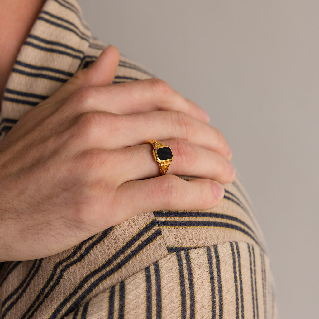 A hand wearing the Vintage Black Signet Ring rests on a shoulder, both dressed in beige and navy striped shirts.