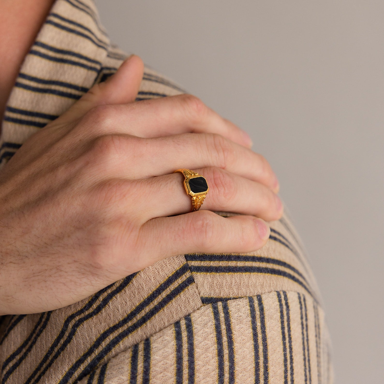 A hand wearing the Vintage Black Signet Ring rests on a shoulder, both dressed in beige and navy striped shirts.