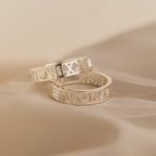 A pair of Roman Numerals Rings in sterling silver with timeless engravings rest on soft beige fabric—ideal as personalized jewelry or a milestone gift to cherish.