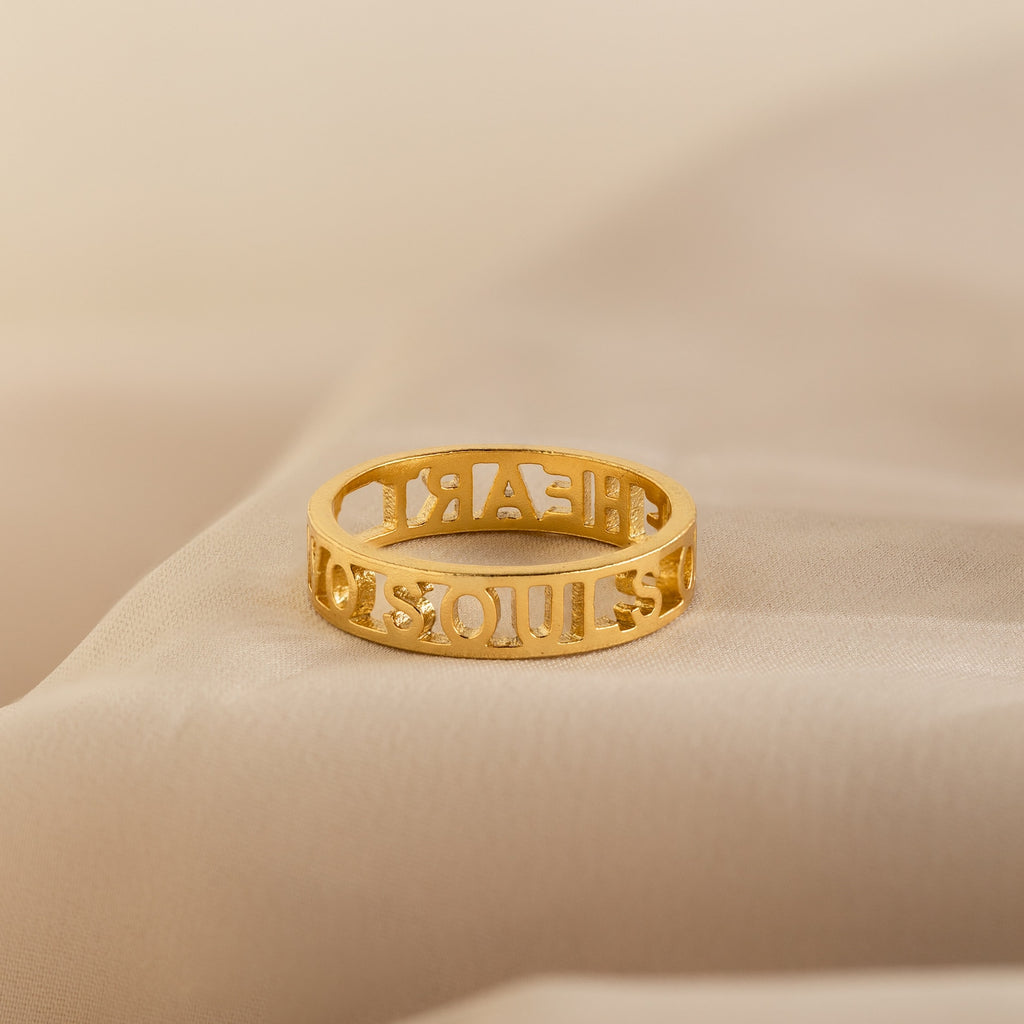 The Roman Numerals Ring, featuring elegant cut-out digits, is shown resting on a soft beige fabric—ideal for personalized milestone jewelry.