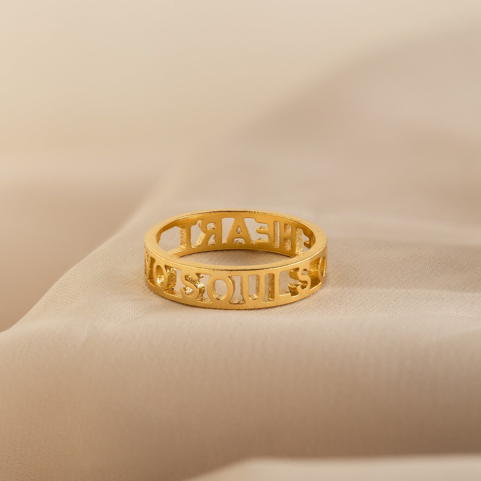 The Roman Numerals Ring, featuring elegant cut-out digits, is shown resting on a soft beige fabric—ideal for personalized milestone jewelry.
