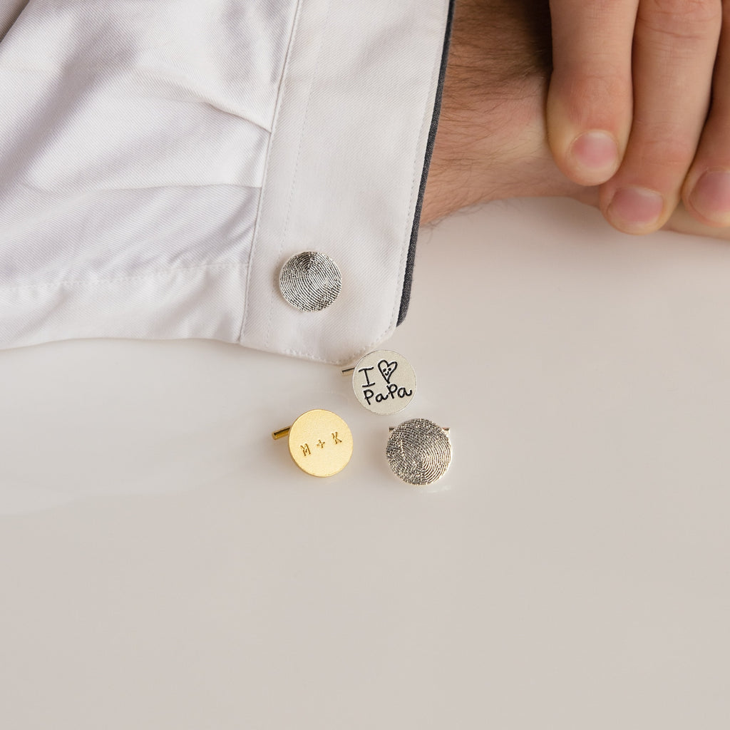 A hand in a white shirt displays three Engraved Cufflinks, one with "I ♥ PaPa" and others with custom designs.