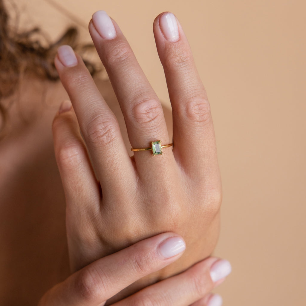 The Agate Emerald Ring shown on a hand against a neutral peach background, emphasizing the vibrant green hue of the gemstone.