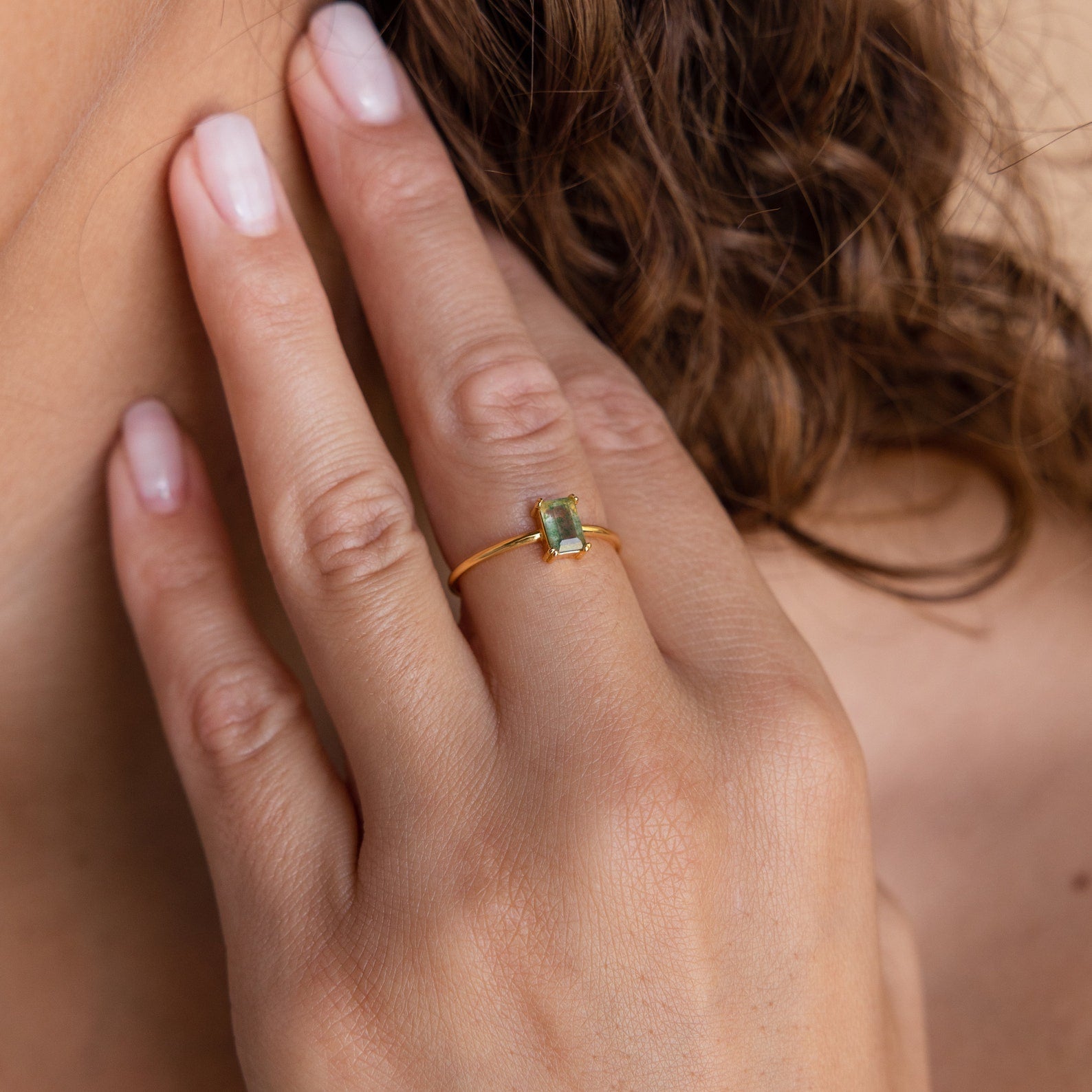 The Agate Emerald Ring worn on a model's finger, showcasing its minimalist gold band and rectangular green gemstone.