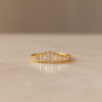 The Art Deco Huggies & Ring Set features a gold ring with a row of rectangular baguette diamonds, inspired by Art Deco jewelry, shown on a smooth light-colored surface.
