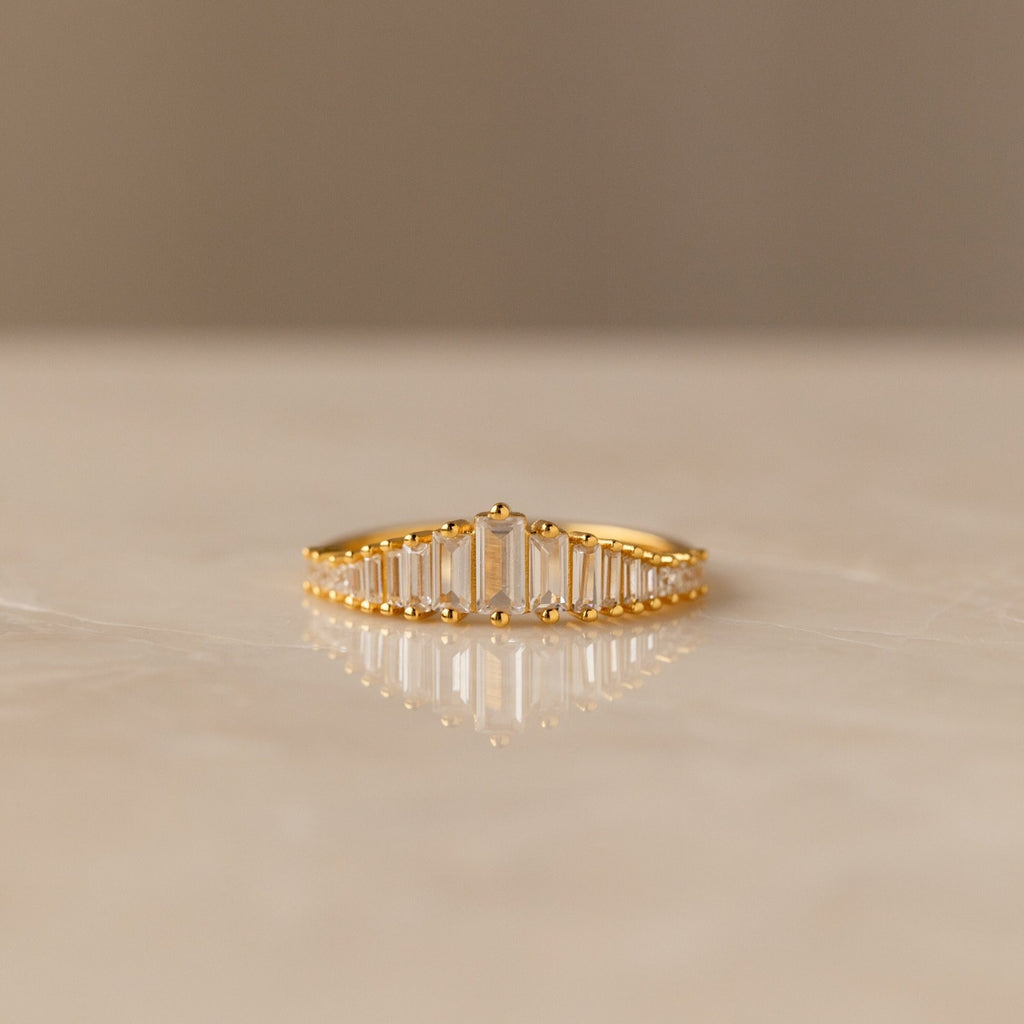 The Art Deco Diamond Earrings & Ring Set in 18K Gold features a gold ring with vertical rectangular stones in a gradual height pattern, evoking vintage elegance, displayed beautifully on marble.