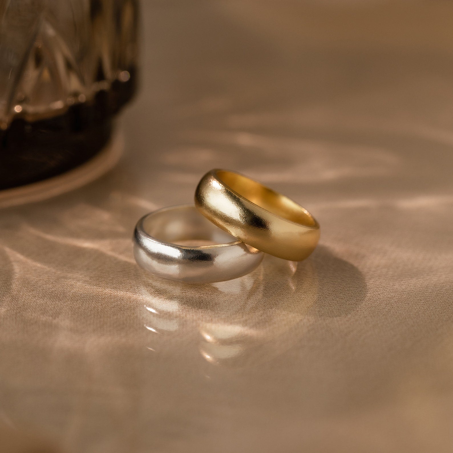 The Thick Half Round Fingerprint Ring—available in silver or gold—rests together on a softly lit beige surface, ideal as minimalist rings or personalized jewelry for everyday elegance.