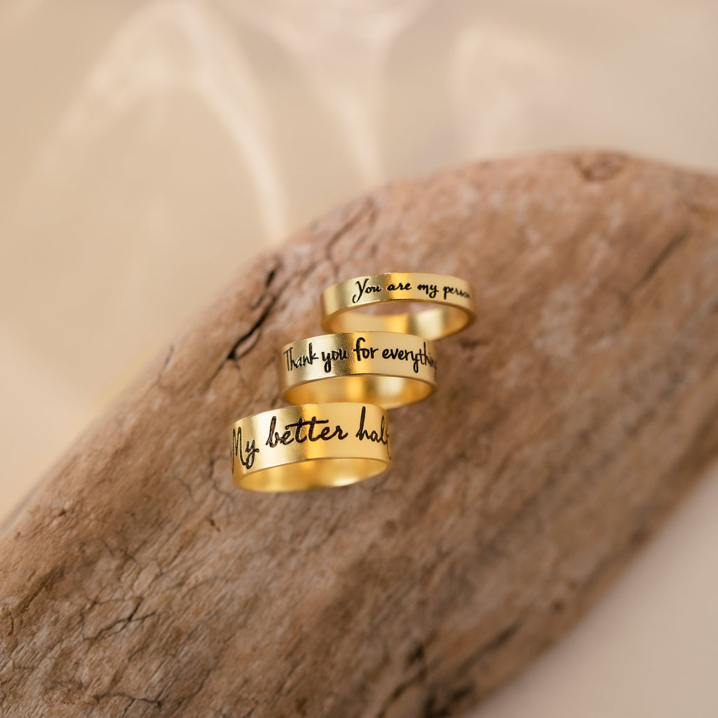 Three Handwriting Bands with engraved messages rest on light brown wood against a soft beige background—the perfect custom ring to treasure as a Christmas gift.