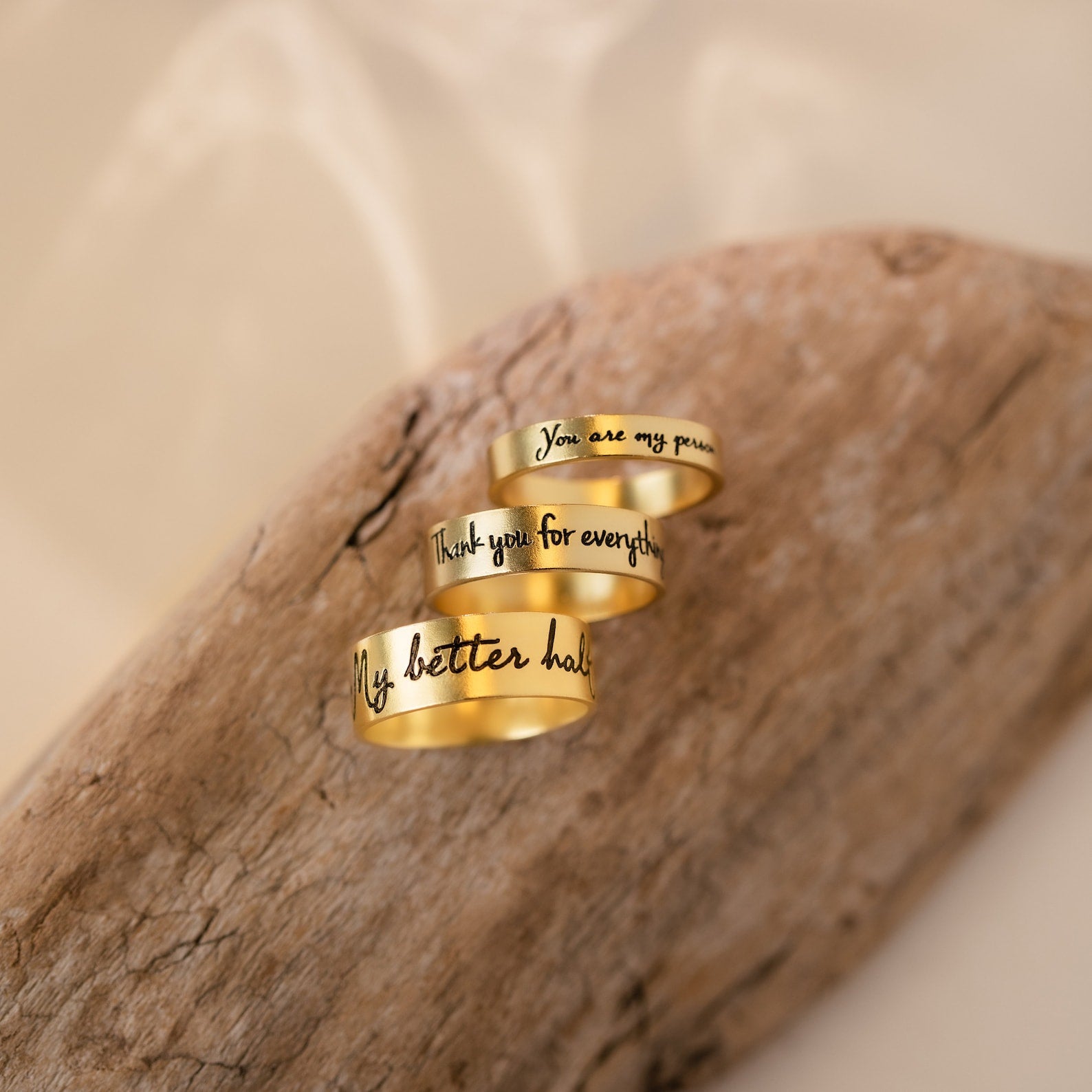 Three Handwriting Bands with engraved messages rest on light brown wood against a soft beige background—the perfect custom ring to treasure as a Christmas gift.