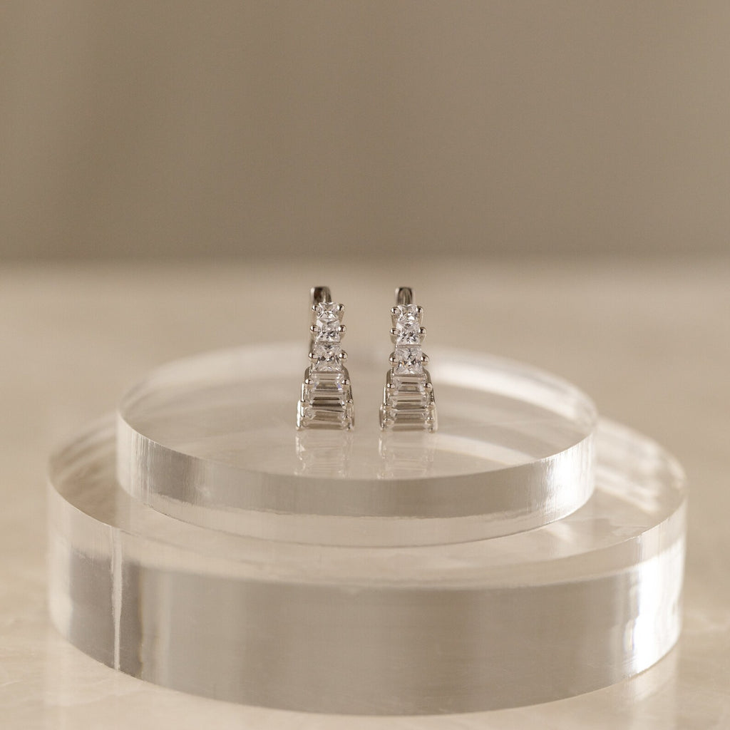Silver Art Deco Huggie earrings displayed on a clear circular stand against a neutral backdrop, highlighting their sculptural design.