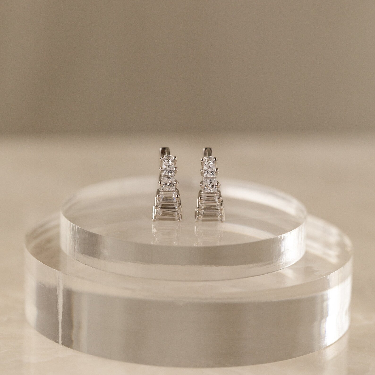 Silver Art Deco Huggie earrings displayed on a clear circular stand against a neutral backdrop, highlighting their sculptural design.