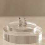 An Art Deco diamond earrings and ring set in sterling silver, elegantly displayed on clear, round acrylic stands against a neutral background.