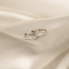 Silver version of the Art Deco Huggie earrings lying on a silky cream surface, emphasizing the clean, icy sparkle of the stones.