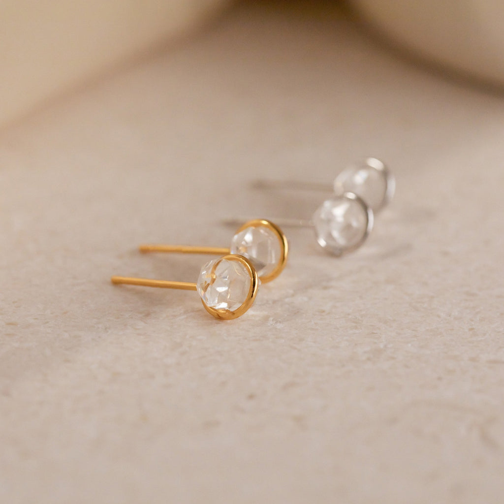 Two pairs of Herkimer Diamond Studs—one in gold, one in silver—each features a clear round gemstone on a textured surface, ideal for an understated look.