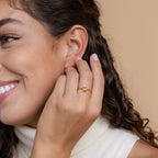 Smiling woman with curly hair wears an elegant Citrine Emerald Ring—her gold band sparkles with a yellow gemstone, the vibrant November birthstone, on her finger.