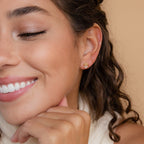 A woman with curly hair smiles, resting her chin on her hand, while wearing minimalist Herkimer Diamond Studs.