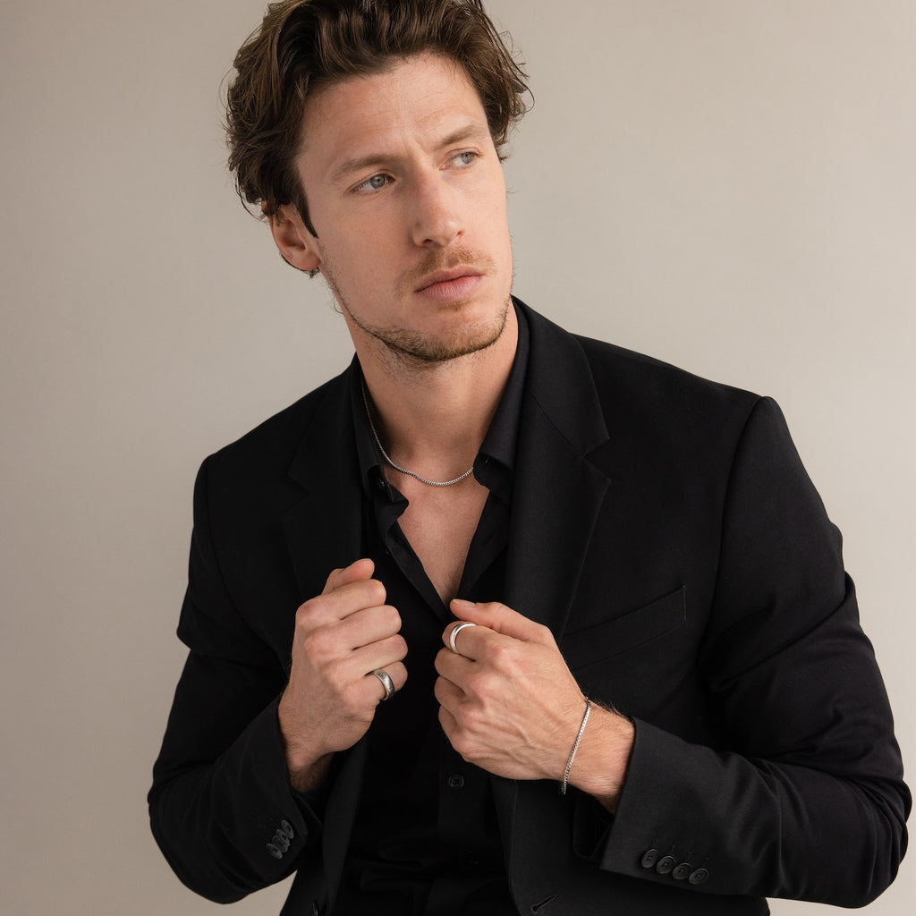 A man in a black suit and shirt wears the Thick Half Round Fingerprint Ring and silver jewelry, gazing to the side against a plain background.