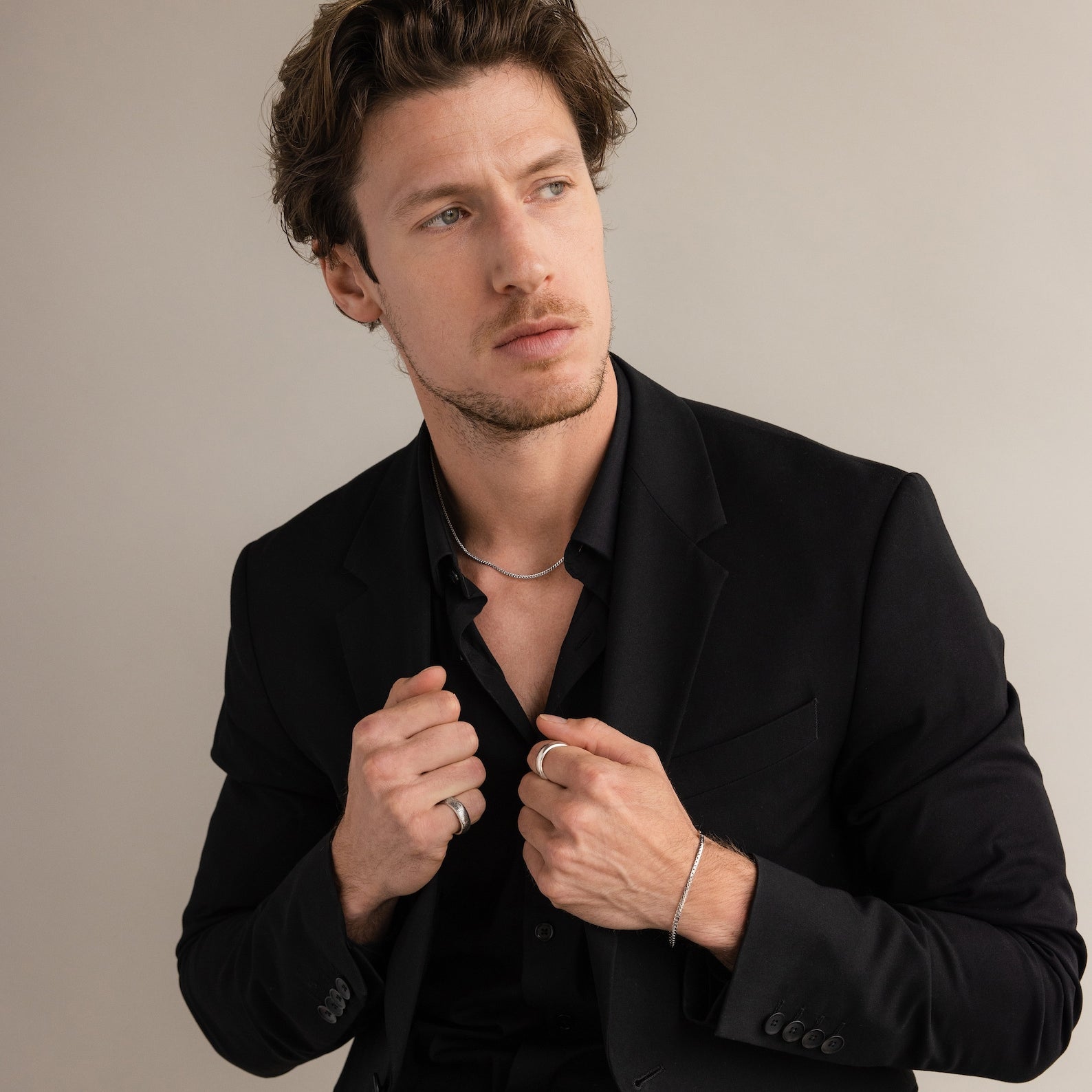 A man in a black suit and shirt wears the Thick Half Round Fingerprint Ring and silver jewelry, gazing to the side against a plain background.