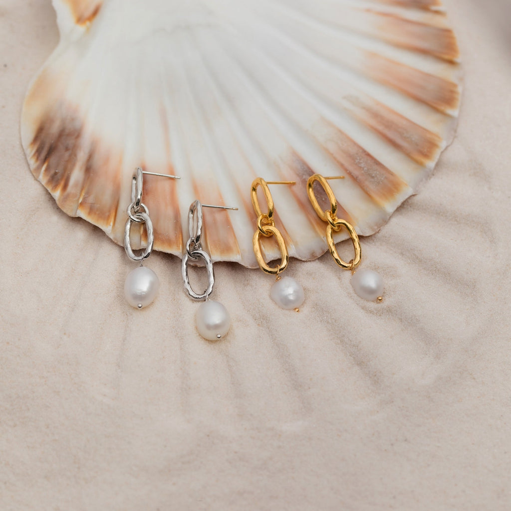 The Pearl Drop Link Studs are elegantly displayed on a seashell.