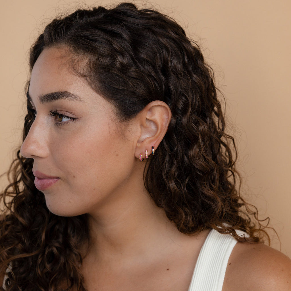 Woman with curly hair wearing Black Opal Inlay Huggies, looking to the left against a beige background.