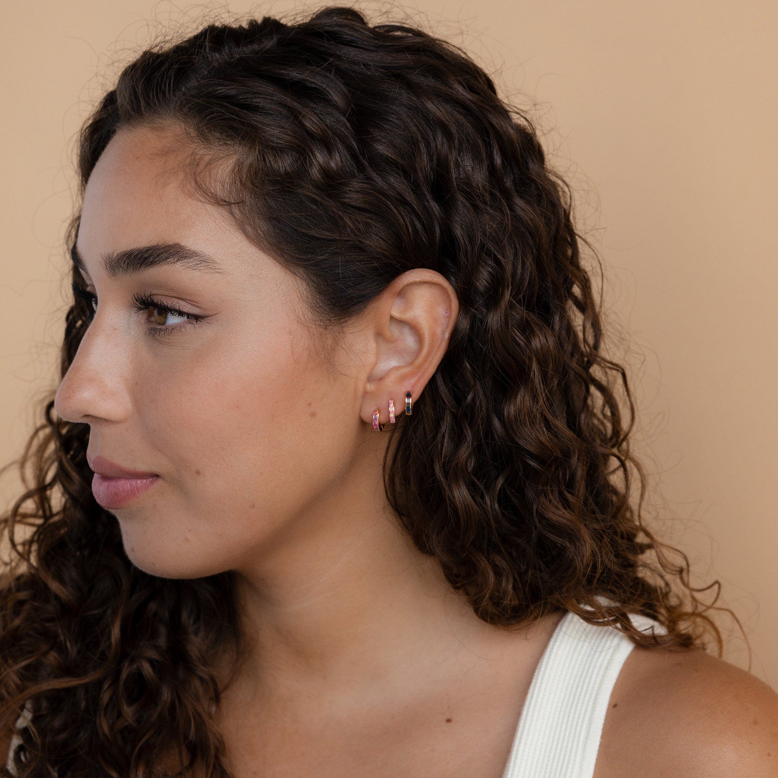Woman with curly hair wearing Black Opal Inlay Huggies, looking to the left against a beige background.