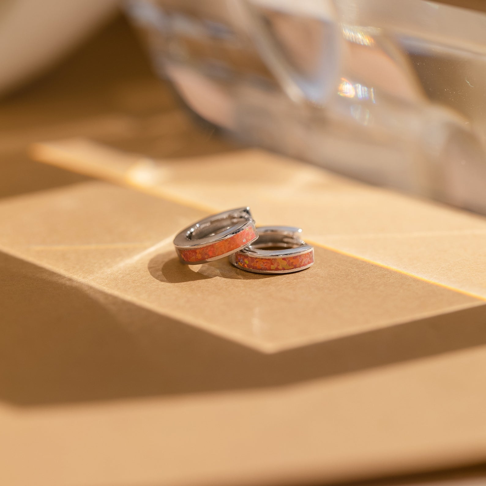 Two Pink Opal Inlay Huggies rest on a beige surface, their silver bands and rosy inlay glowing softly in natural light.