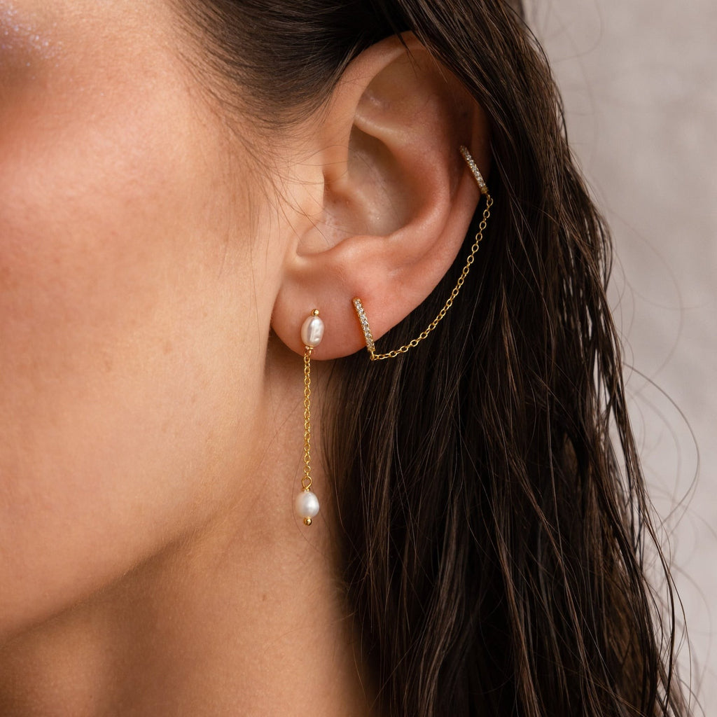 Close-up of a woman’s ear wearing Pearl Drop Chain Earrings—minimalist earrings with pearls and a fine chain linking two piercings.
