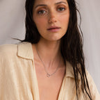 A woman with wet hair in a beige shirt wears the Rolo Circle Charm Necklace in Sterling Silver, looking at the camera with a neutral expression. This customizable necklace elevates her simple, elegant style.