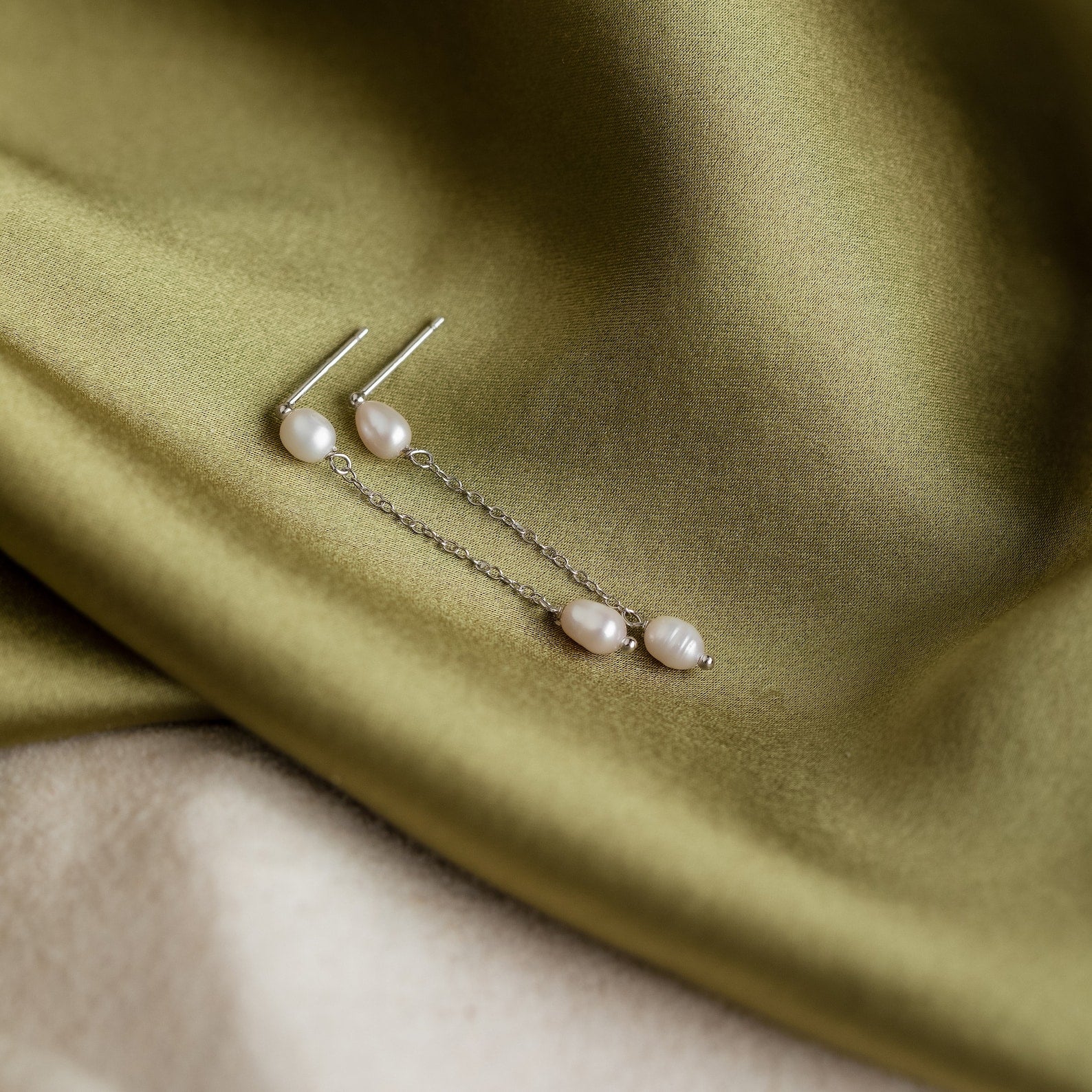 Pearl Drop Chain Earrings with silver chains rest elegantly on light olive green satin, making them perfect for a minimalist earrings collection.