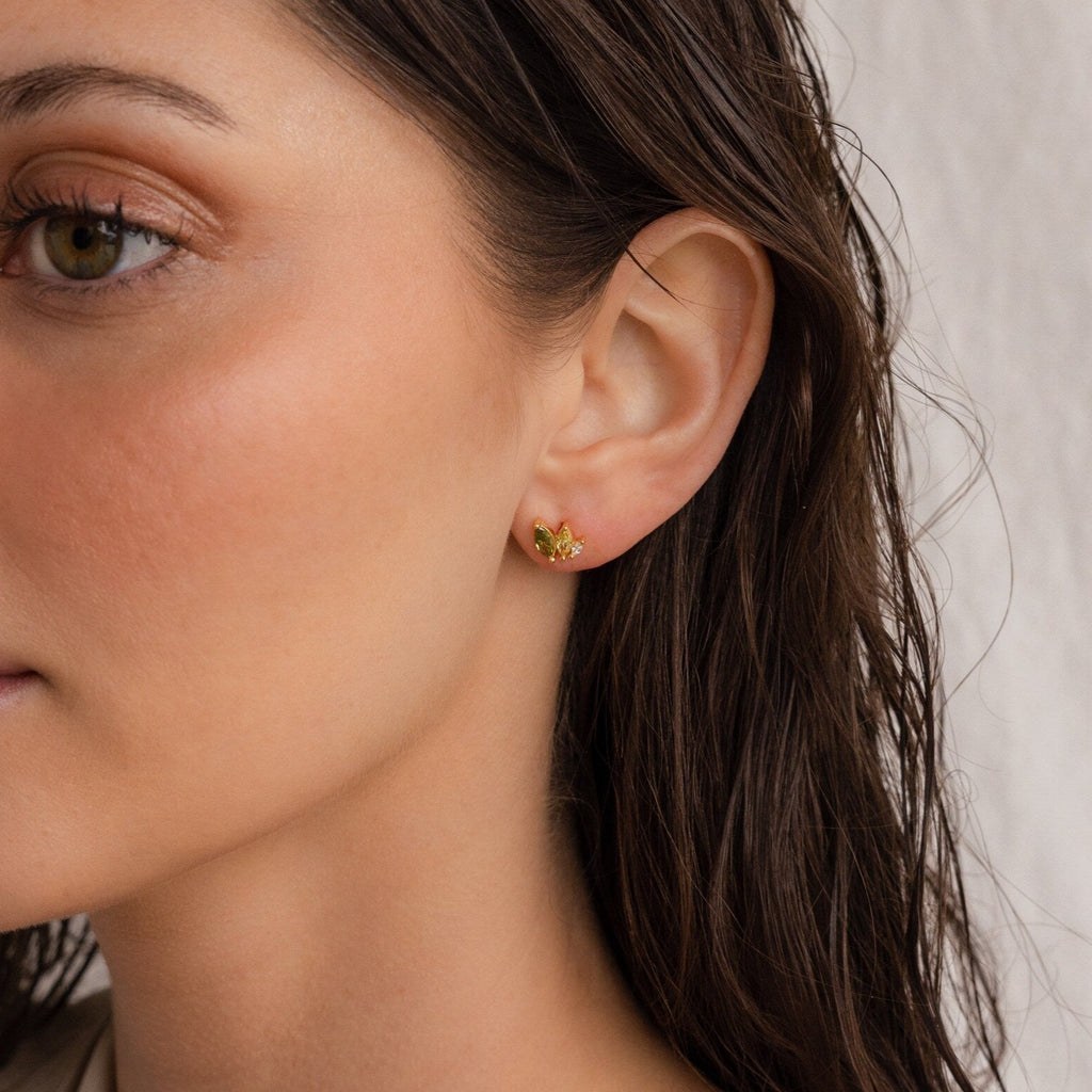 Woman with wet brown hair wearing Seagrass Peridot Marquise Studs—small gold gemstone earrings shaped like leaves and flowers.