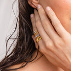 A hand with nude nails touches wet hair, showcasing three gold rings with ocean-blue gemstones, including the elegant Aquamarine Stacking Ring Set.