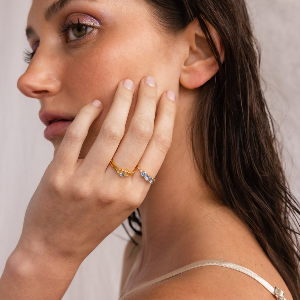 Woman with wet hair wearing boho rings, including the Aquamarine Stacking Ring Set with ocean blue gemstones, touches her face softly under gentle lighting.